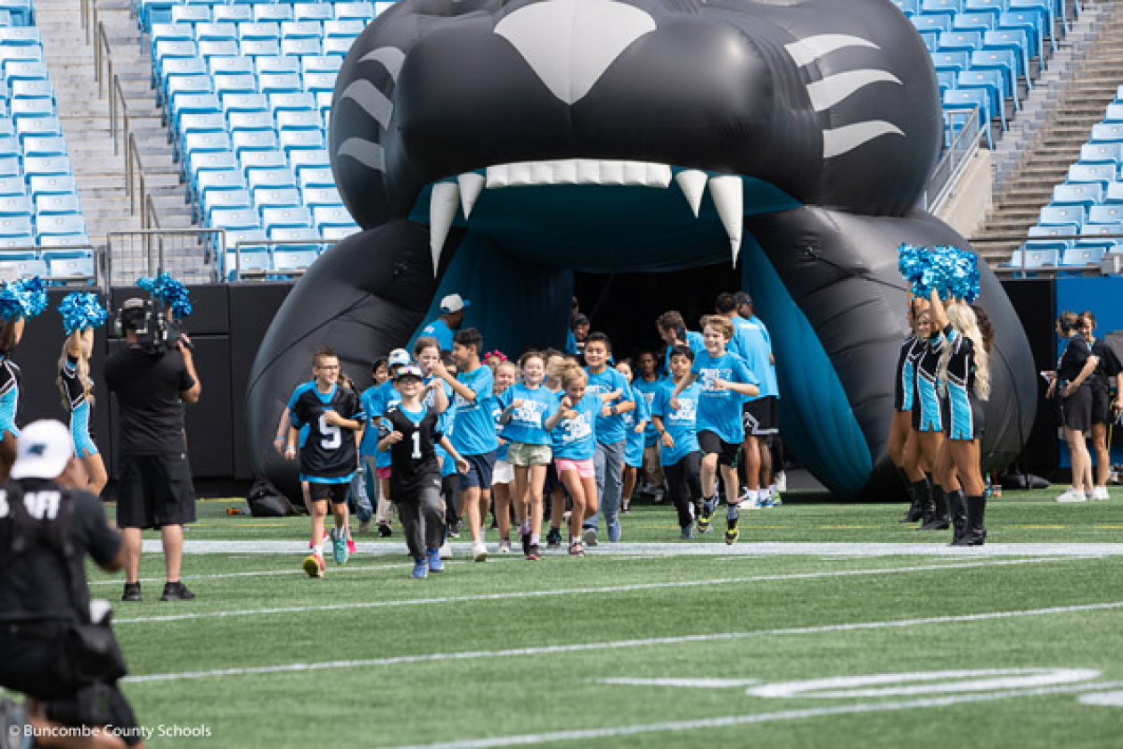 W.D. Williams students, dressed in Panthers gear, run out of a panther mouth tunnel onto the field.