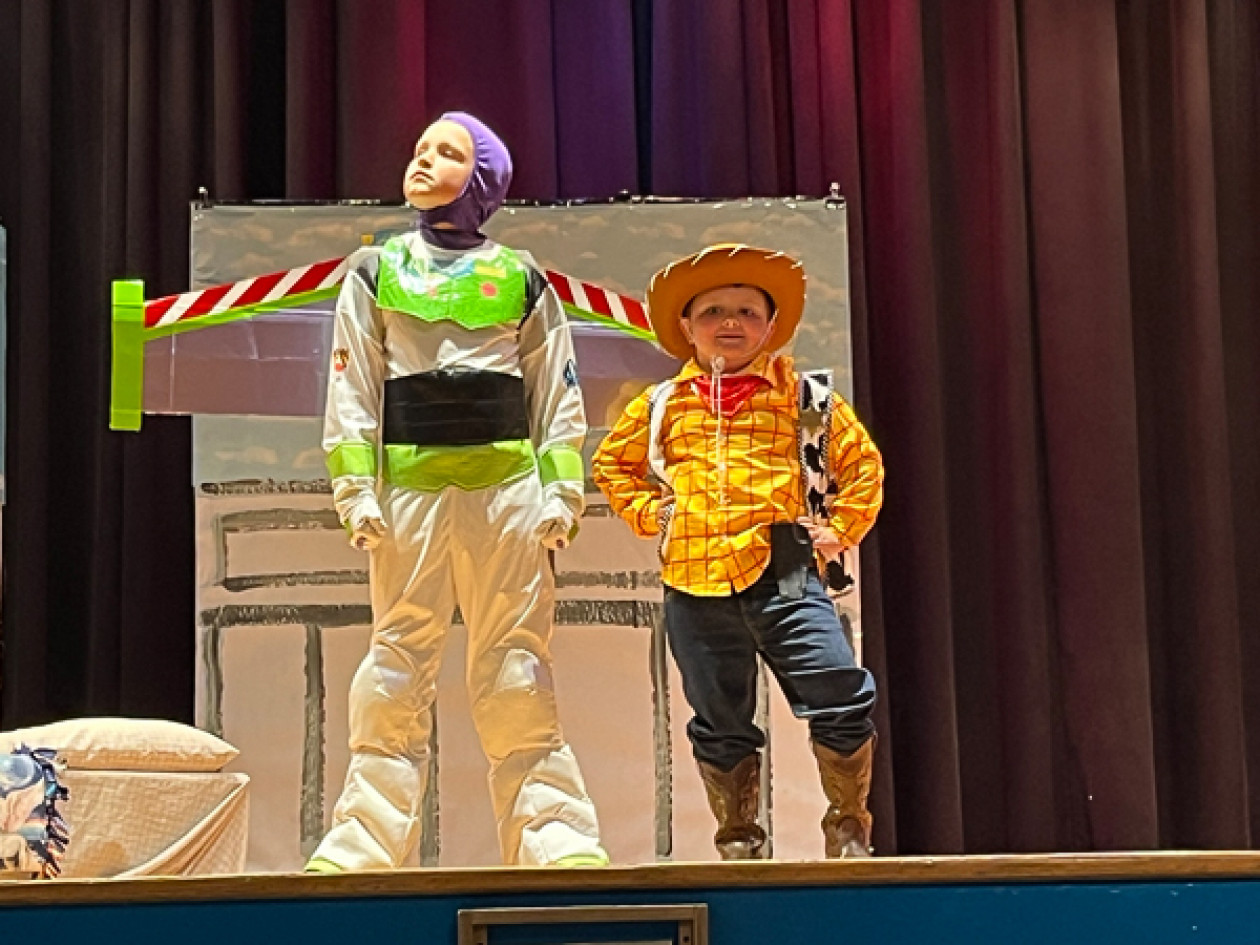 Students dressed as Buzz Lightyear and Woody from Toy Story pose on stage.