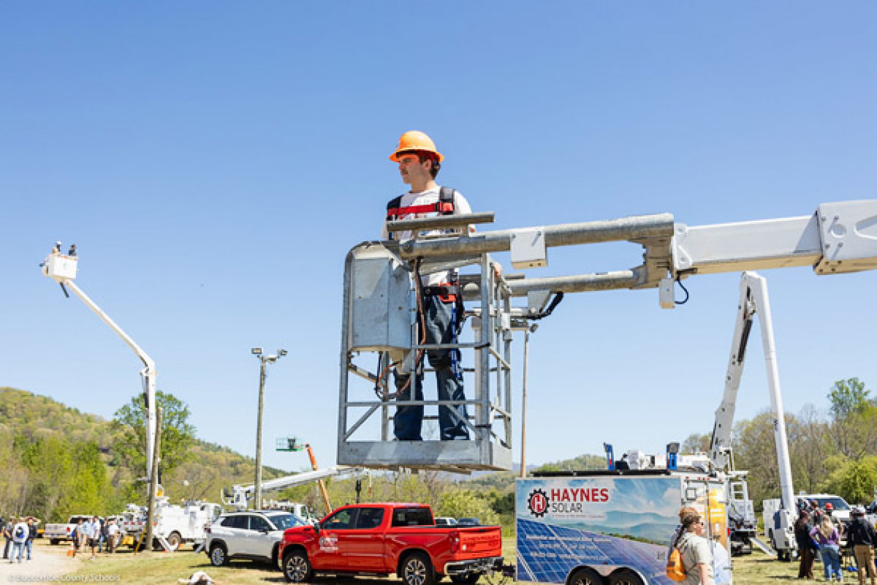 A student looks to his right as he stands in a utility truck's bucket.