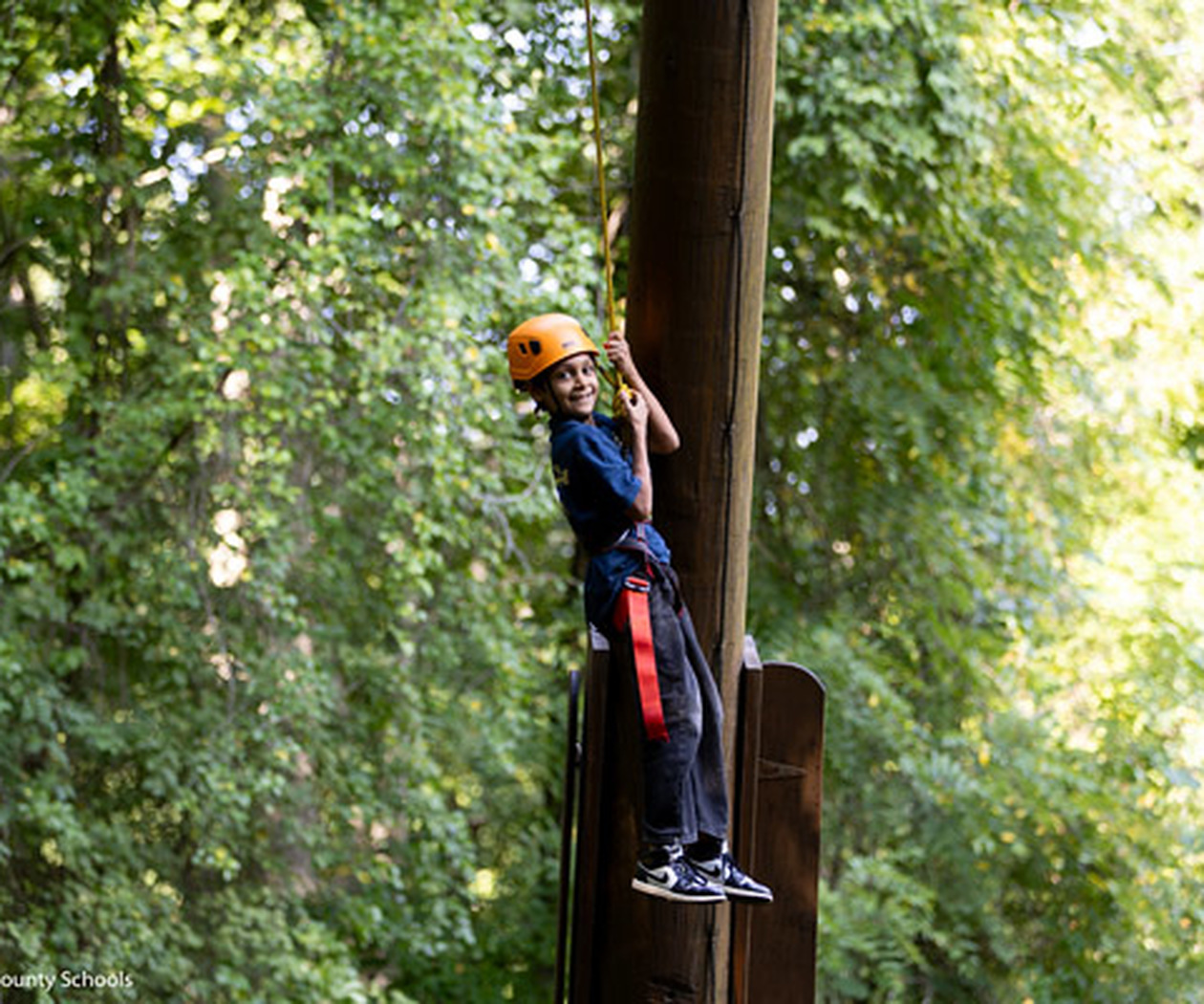 A student smiles while riding a zip line.