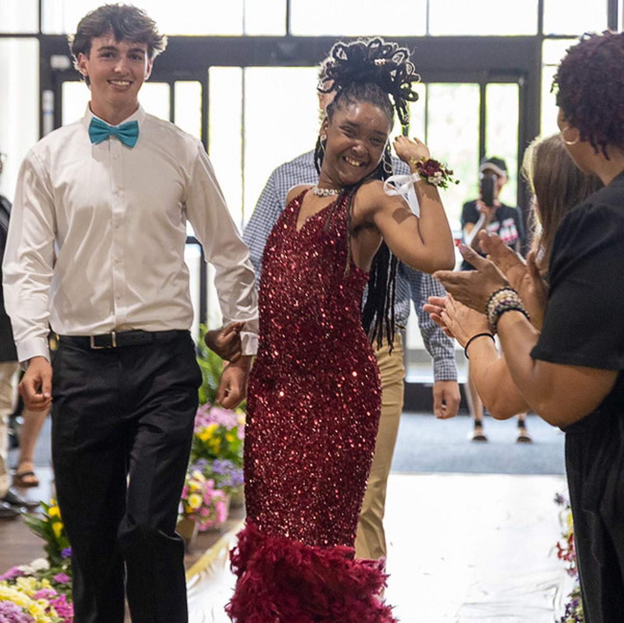 Students wearing prom attire smile as they walk down an entryway.