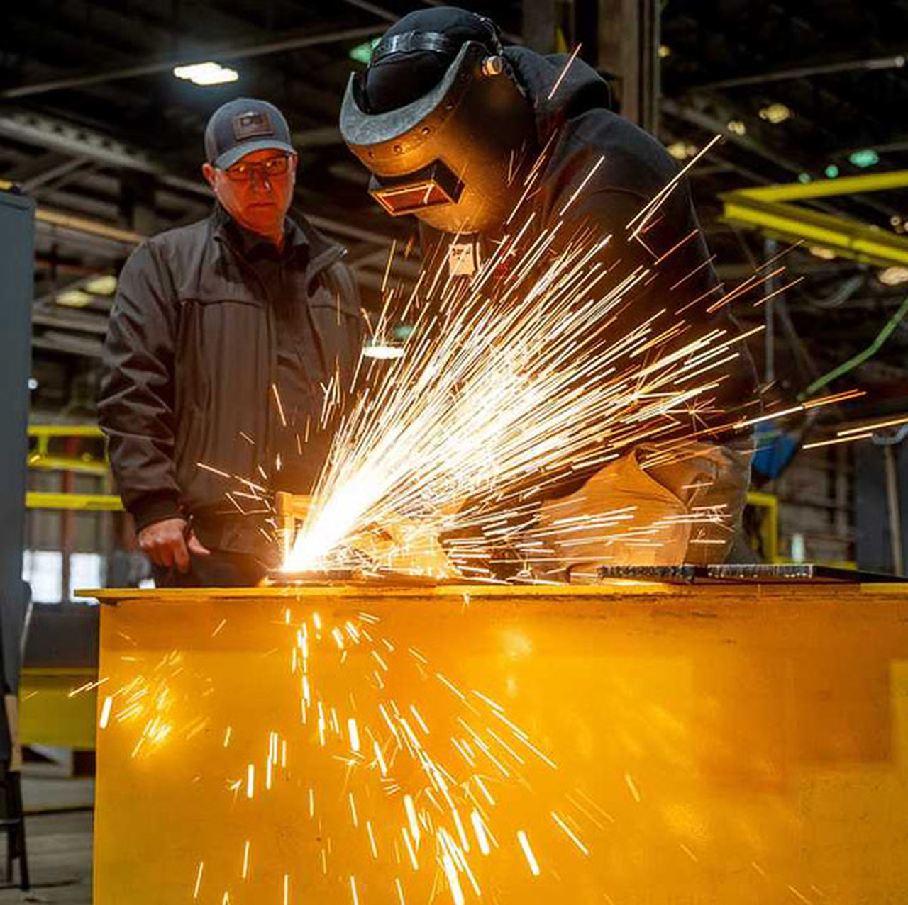 Sparks fly as a student welds while a teacher watches.