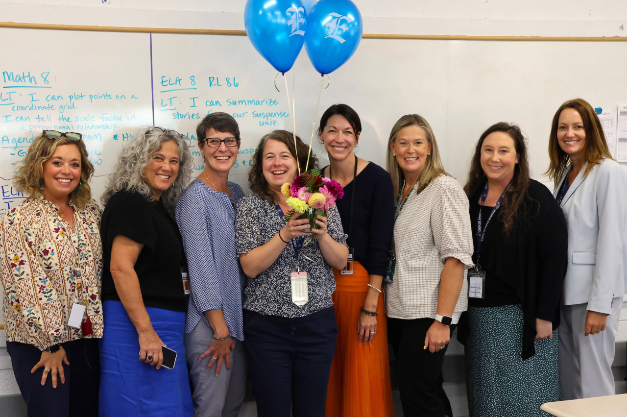Chelsea Myer holds balloons and flowers while surrounded by school and district leaders.