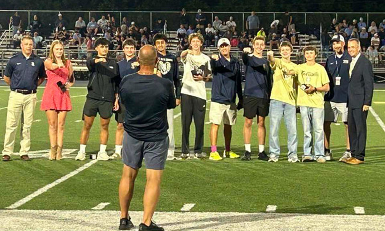 Athletes hold out their rings while standing on the football field.