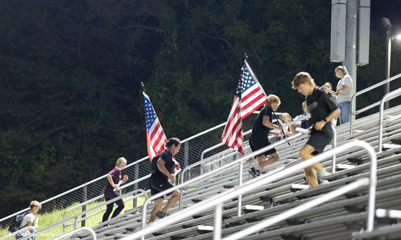 A group of students carry American flags up the bleachers.