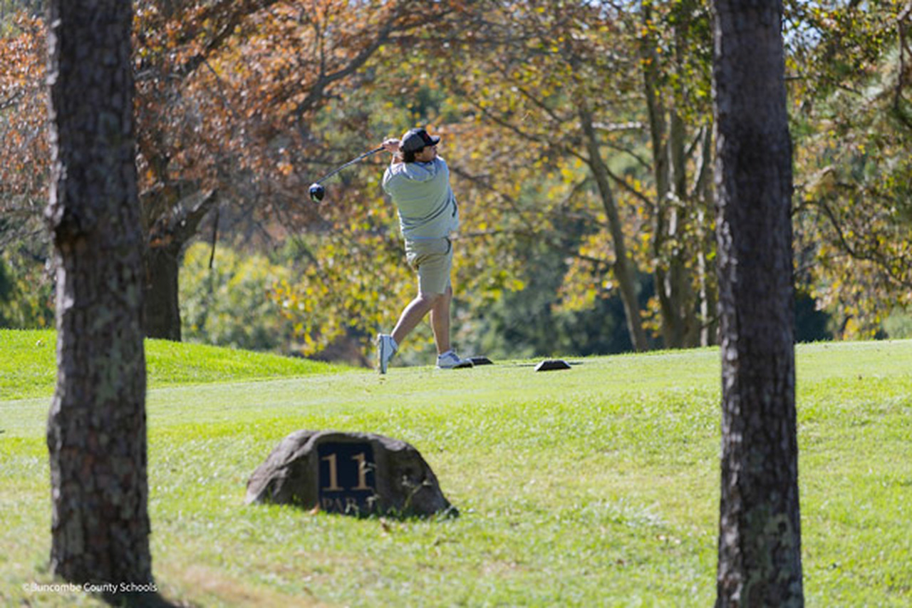A golfer swings a driver at the course.