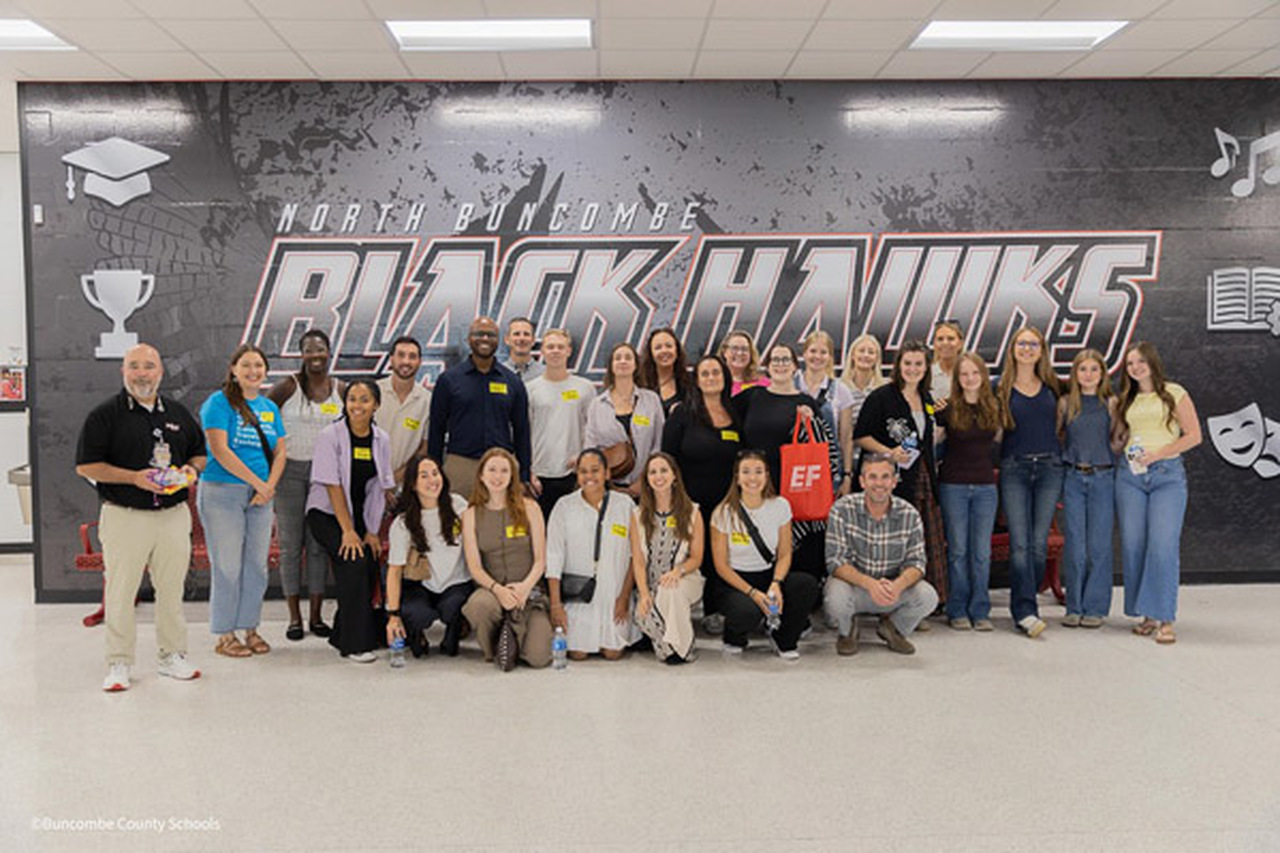 EF Exchange Ambassadors pose with school leadership and students in front of a North Buncombe High wall mural.
