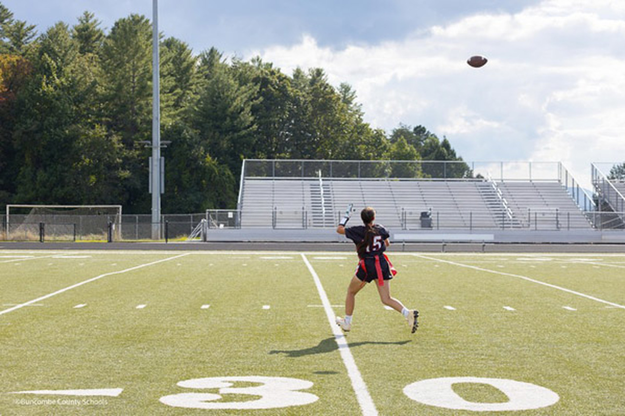 A flag football player reaches up to catch a ball.