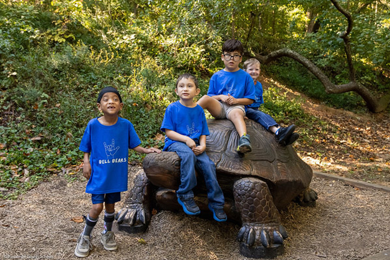 Four students wearing blue shirts sit on a turtle sculpture.