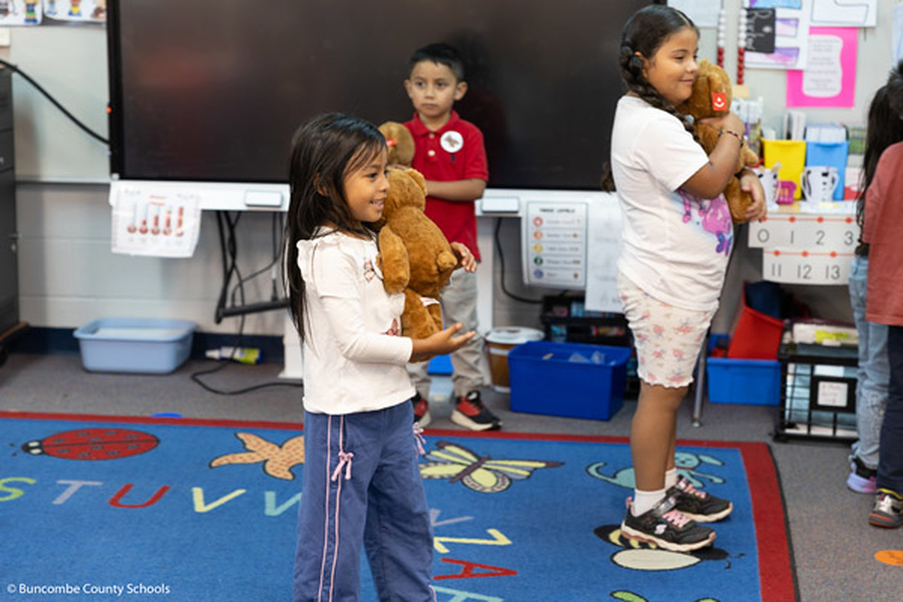 Two girls and a boy hold teddy bears.