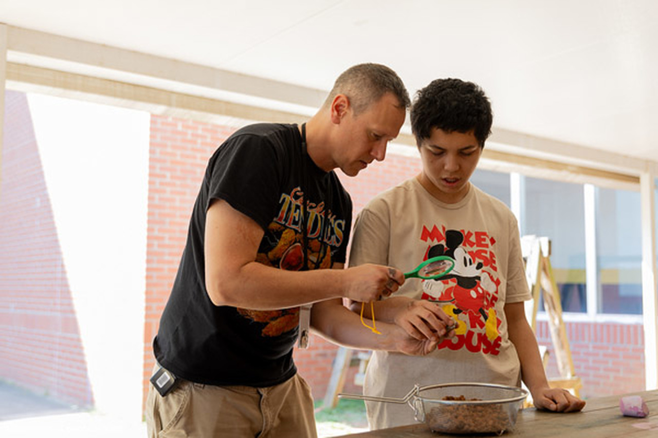 Thomas Mensch holds a magnifying glass as a student looks.
