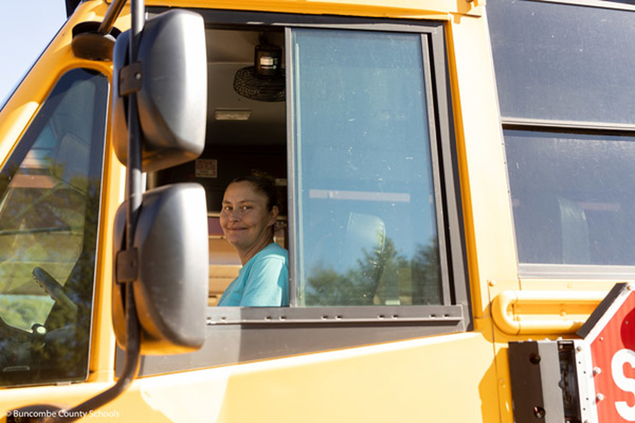 Cassie Whitaker smiles while sitting in the driver seat of a school bus.