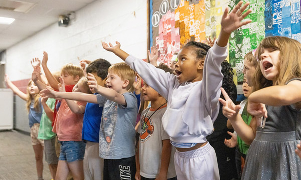 Students raise their hands in the air while singing a song.