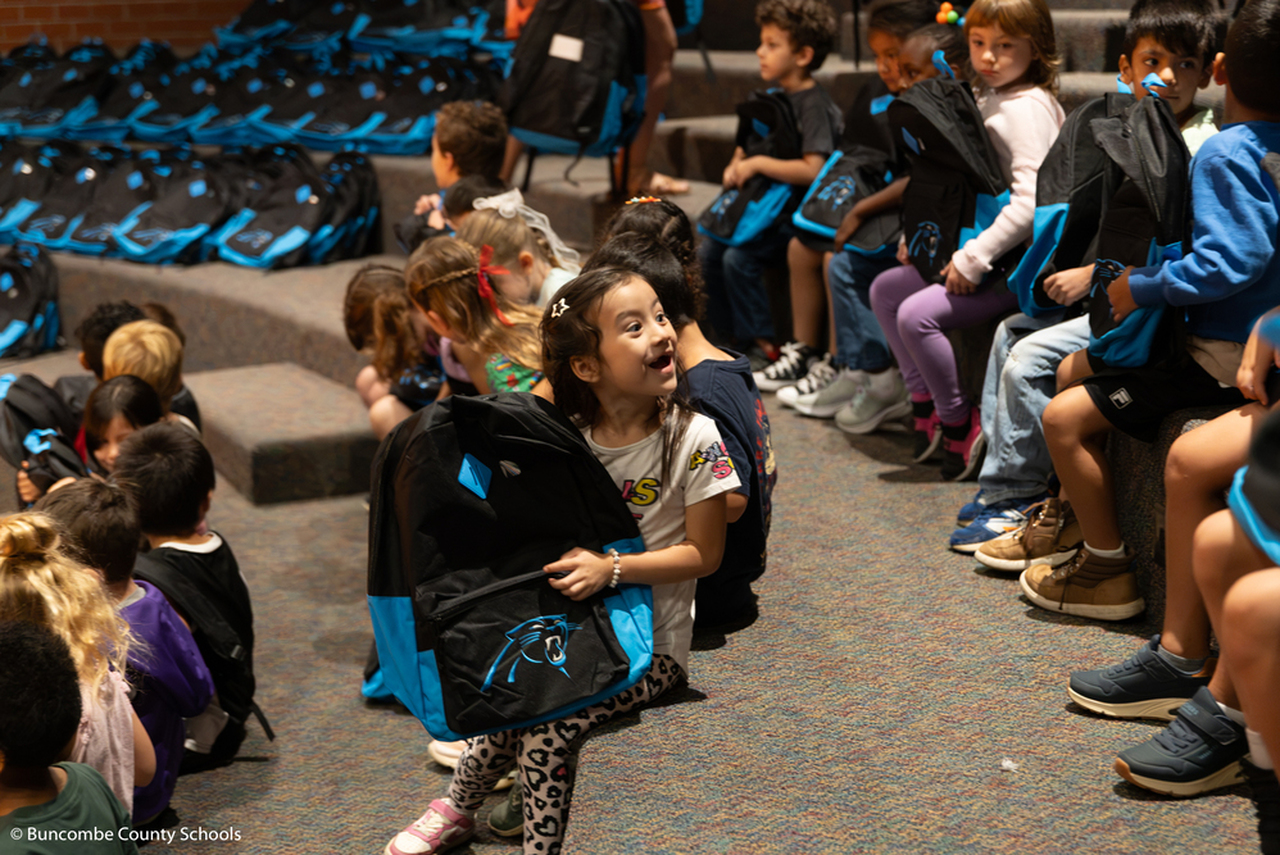 A girl looks over her shoulder and smiles while holding a Carolina Panthers backpack.