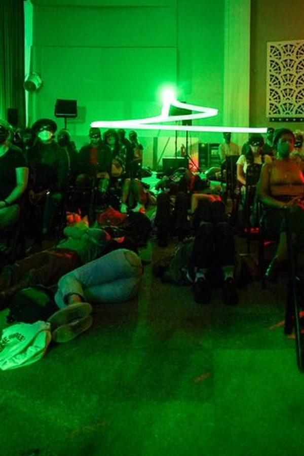 People sit and lay in a dark room with green and red fluorescent lights