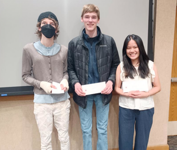 Three students stand next to each other, each holding white paper certificates