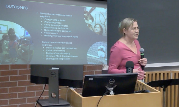 Julie Neiworth stands in a pink shirt with a microphone in front of a classroom podium