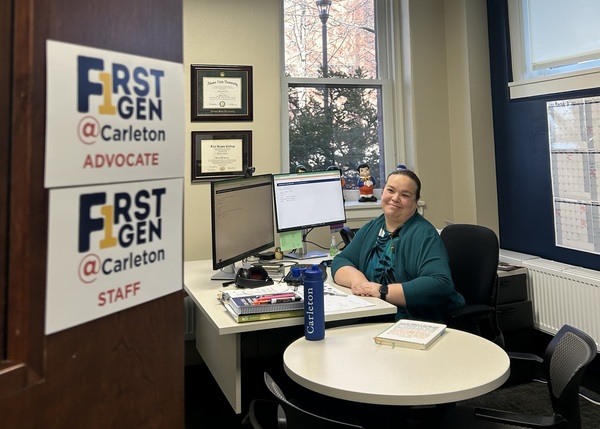 Person smiles from desk with door adorned with First Gen advocate card