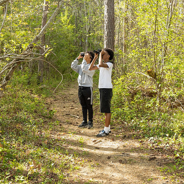 Two boys look through binoculars as they stand on a trail on the A.C. Reynolds Middle campus.
