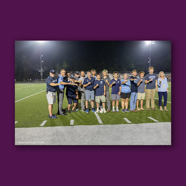 Enka High wrestlers, along with school and district leaders, stick their fists out to show off their rings while standing on the football field.