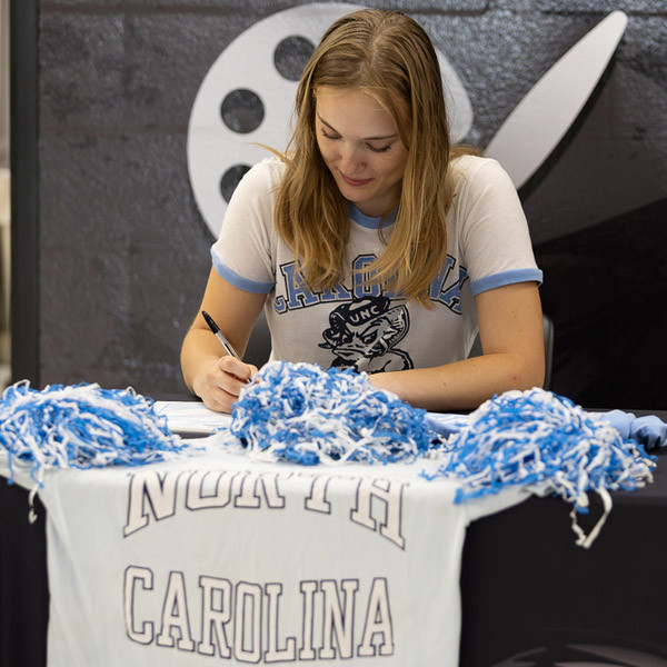 A senior signs while wearing UNC Chapel Hill attire and surrounded by UNC colors.