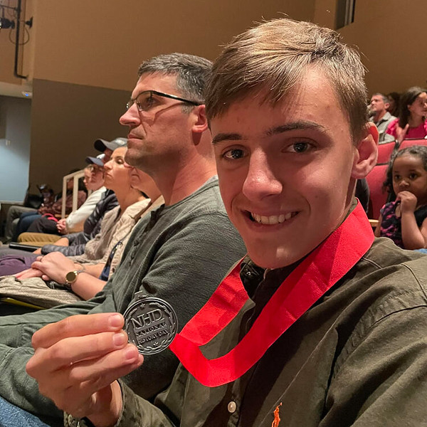 Alex Ermuache holds up his medal while smiling.