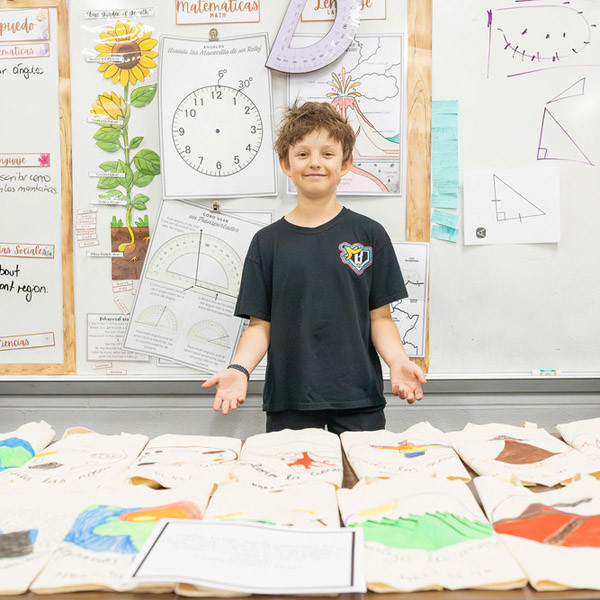 A boy spreads his hands to show recyclable canvas bags with hand-drawn designs.