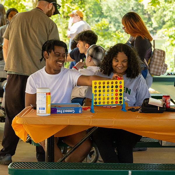 Two students play Connect 4 in a picnic shelter at Lake Julian Park..