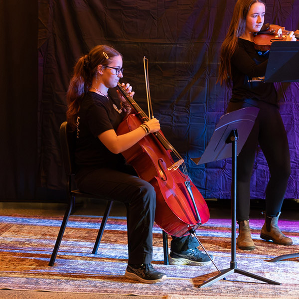 A student plays the cello on a stage.