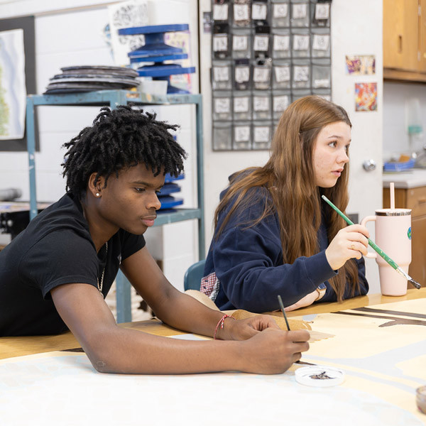 A boy and a girl work on painting designs for the mural.