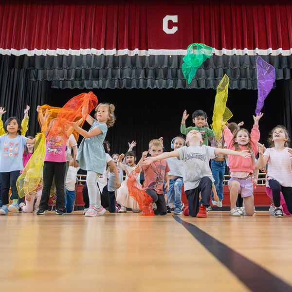 Kindergarten students throw colored fabric in the air at the end of a dance routine.