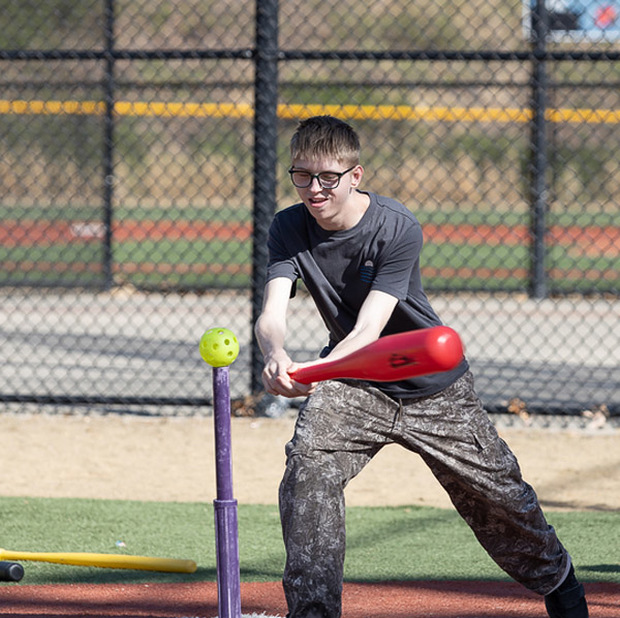 A student hits a wiffle ball off of a tee.