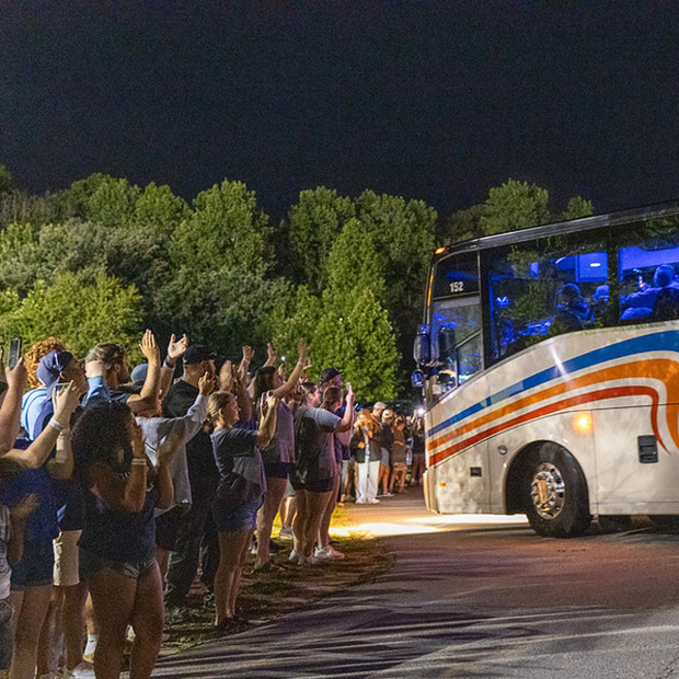 People clap and wave as a charter bus arrives at Enka High School.