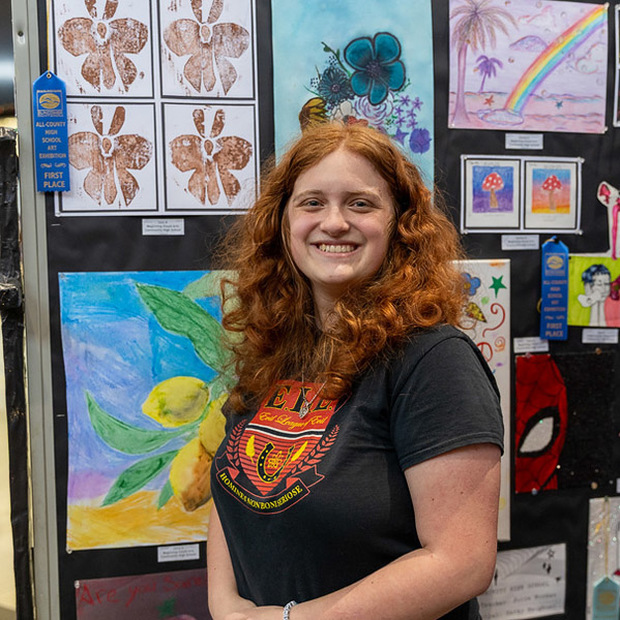 A student poses in front of a blue ribbon art piece.
