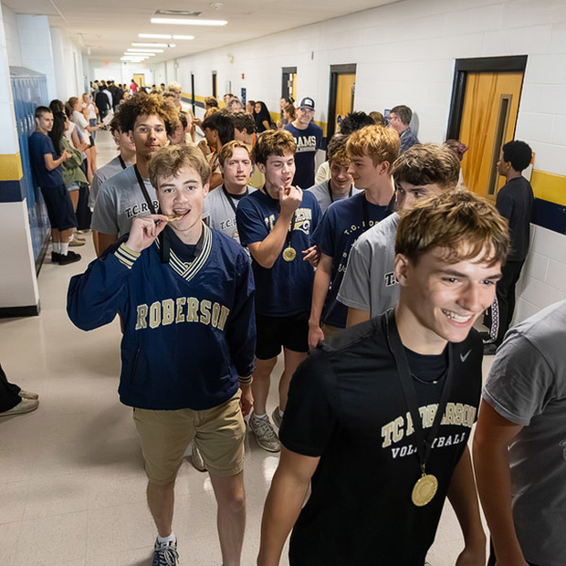 A volleyball player bites his medal while the parade walks down the hall.