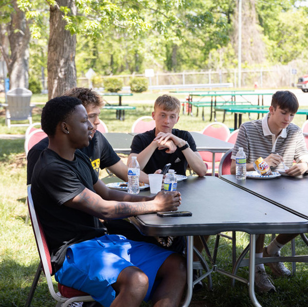 Students sit outside at a table while eating lunch.