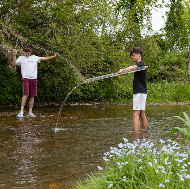 One student pours out a water sample into the creek as another walks in the streambed.