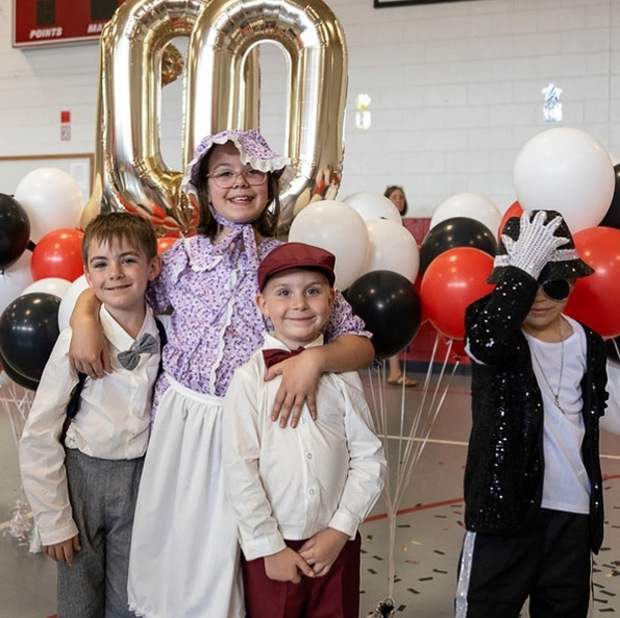 Four students, dressed in clothing from the last 100 years, pose in front of balloons.